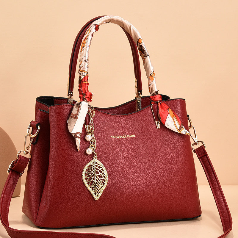 Red handbag with decorative handle and leaf charm on a beige background